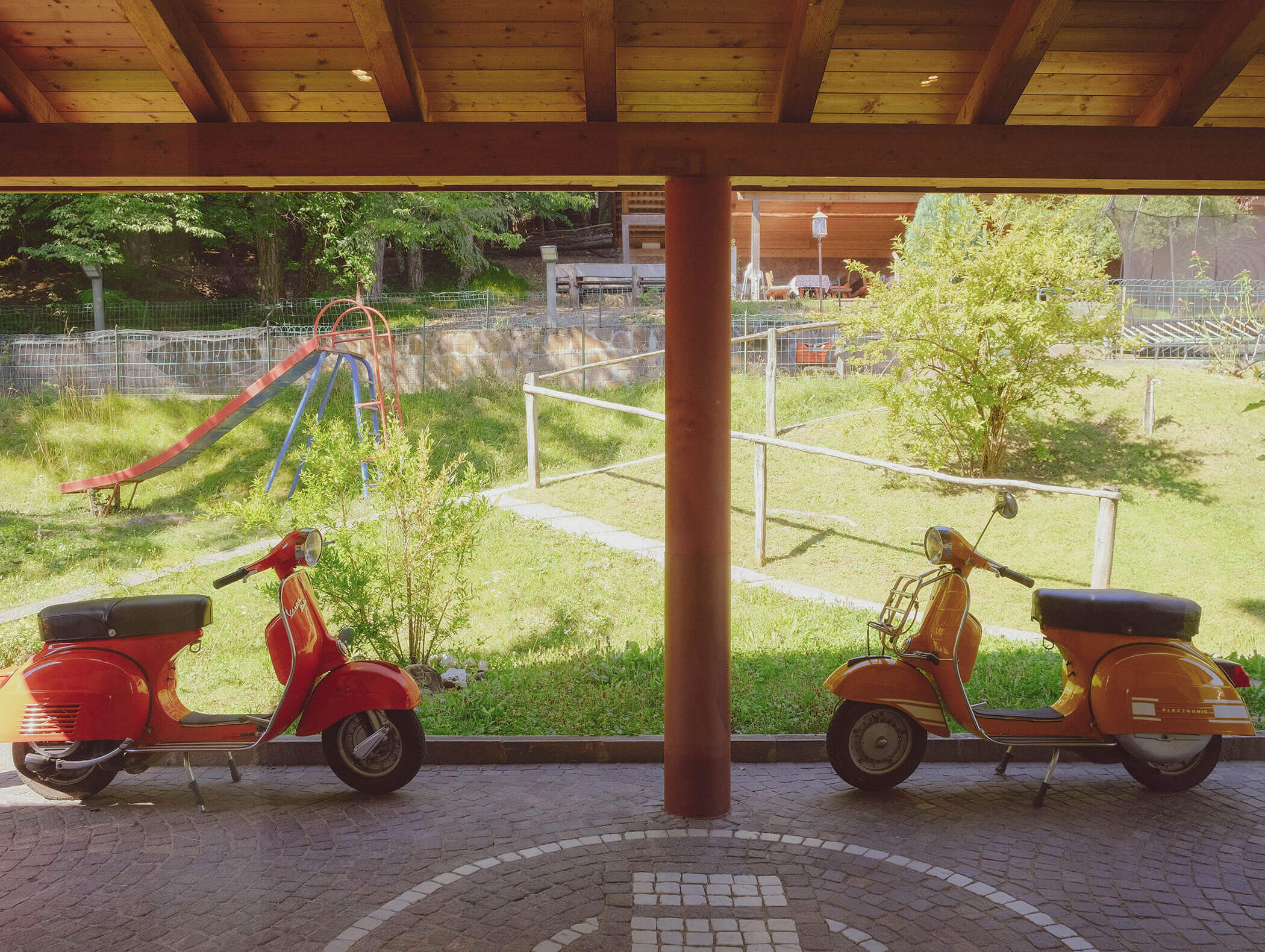 Zwei Oldtimer-Roller, die unter einem Holzdach geparkt sind, mit einem grasbewachsenen Spielplatz und einer Rutsche im Hintergrund. - Wandergasthof Steinegger