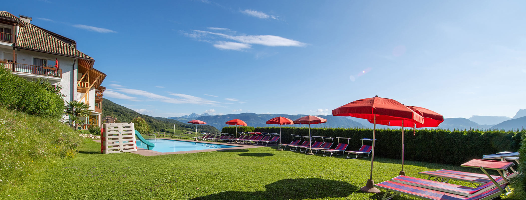 Un'area a bordo piscina con ombrelloni rossi, sedie a sdraio e vista sulle montagne nelle giornate di sole. - Wandergasthof Steinegger