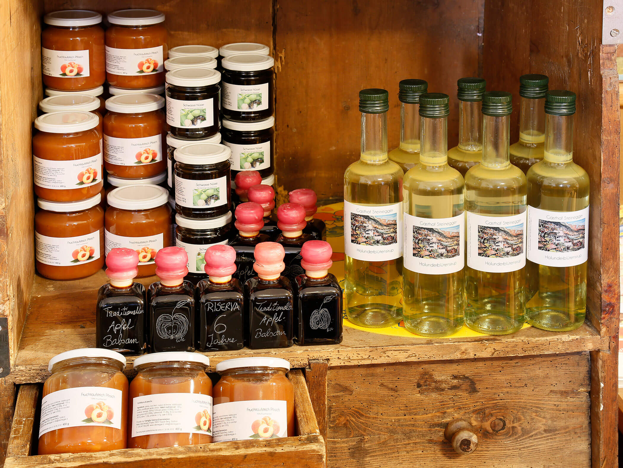 Barattoli di conserve e bottiglie di liquido giallo esposti su scaffali di legno in una credenza rustica. - Wandergasthof Steinegger