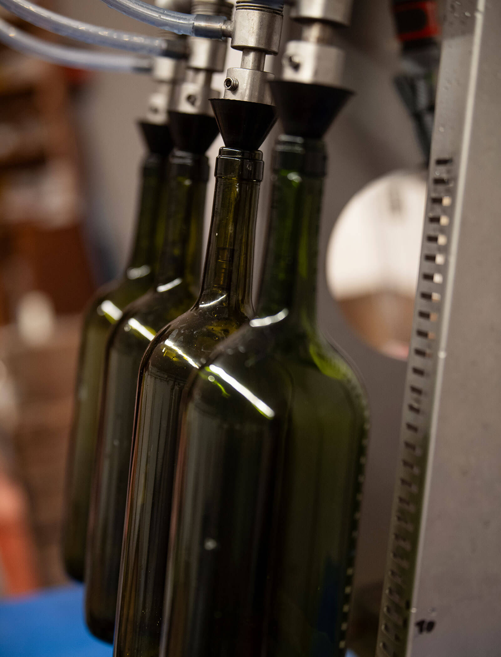 Tre bottiglie di vetro verde riempite da una macchina automatica per l'erogazione di liquidi in un ambiente industriale. - Wandergasthof Steinegger
