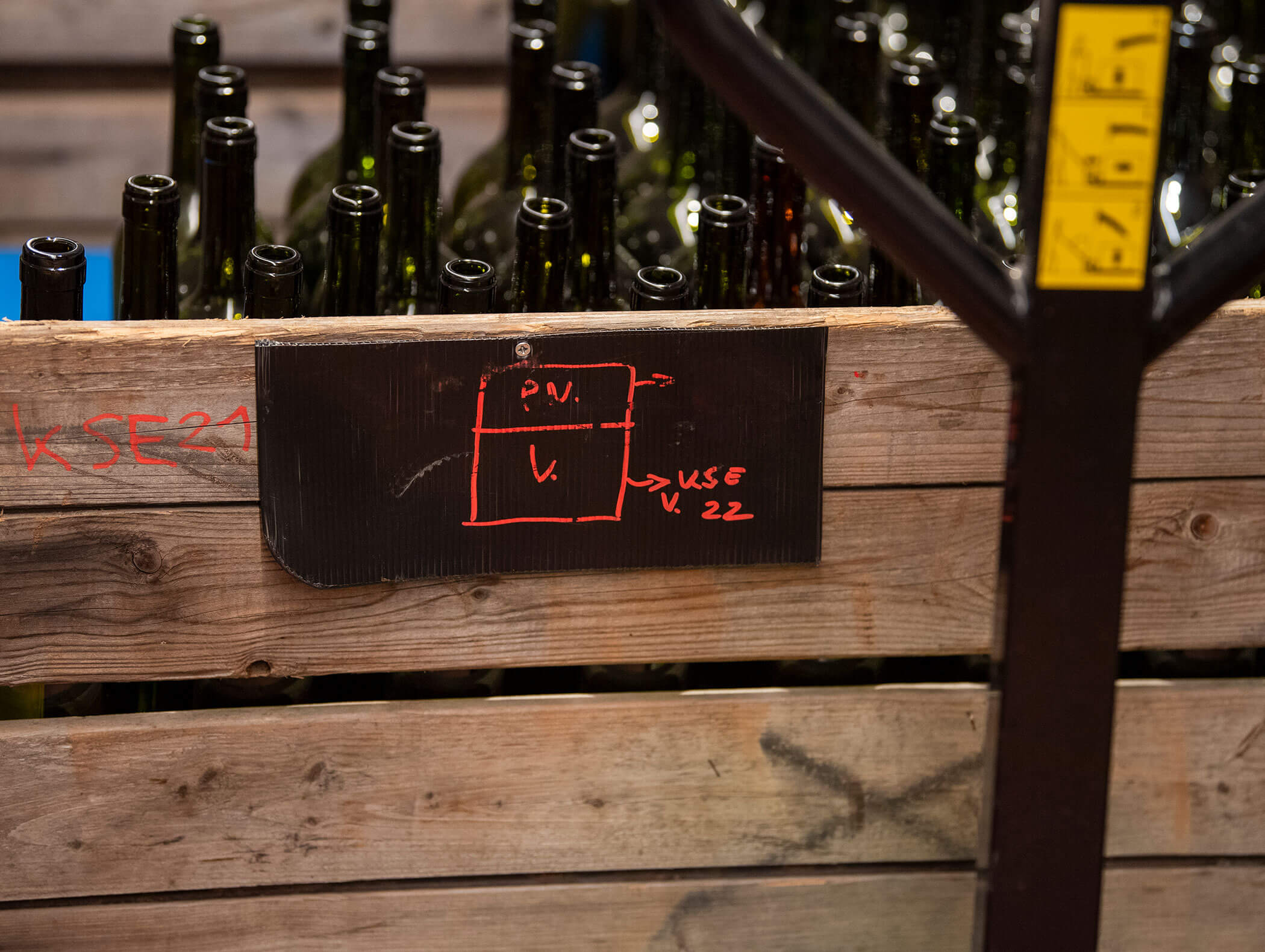 Cassa di legno piena di bottiglie di vetro vuote, etichettate con un diagramma rosso disegnato a mano su un cartello nero. - Wandergasthof Steinegger
