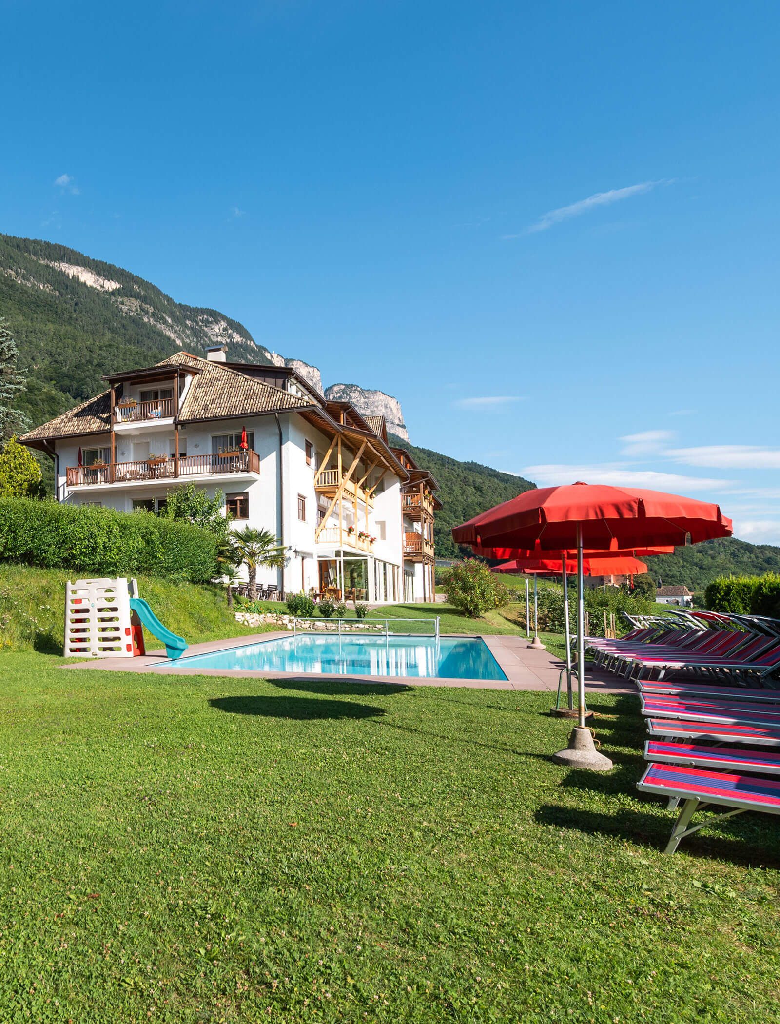 Ein Hotel mit Balkonen mit Blick auf einen Pool, Liegestühle und Berge unter einem klaren blauen Himmel. - Wandergasthof Steinegger
