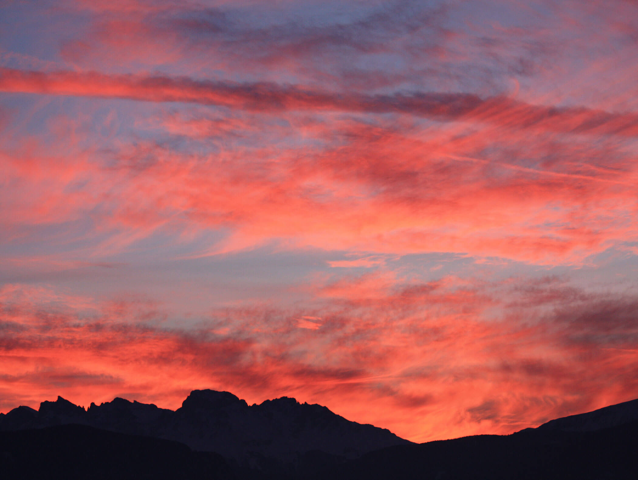 Pink and orange clouds at sunset above silhouetted mountains against a blue sky. - Wandergasthof Steinegger