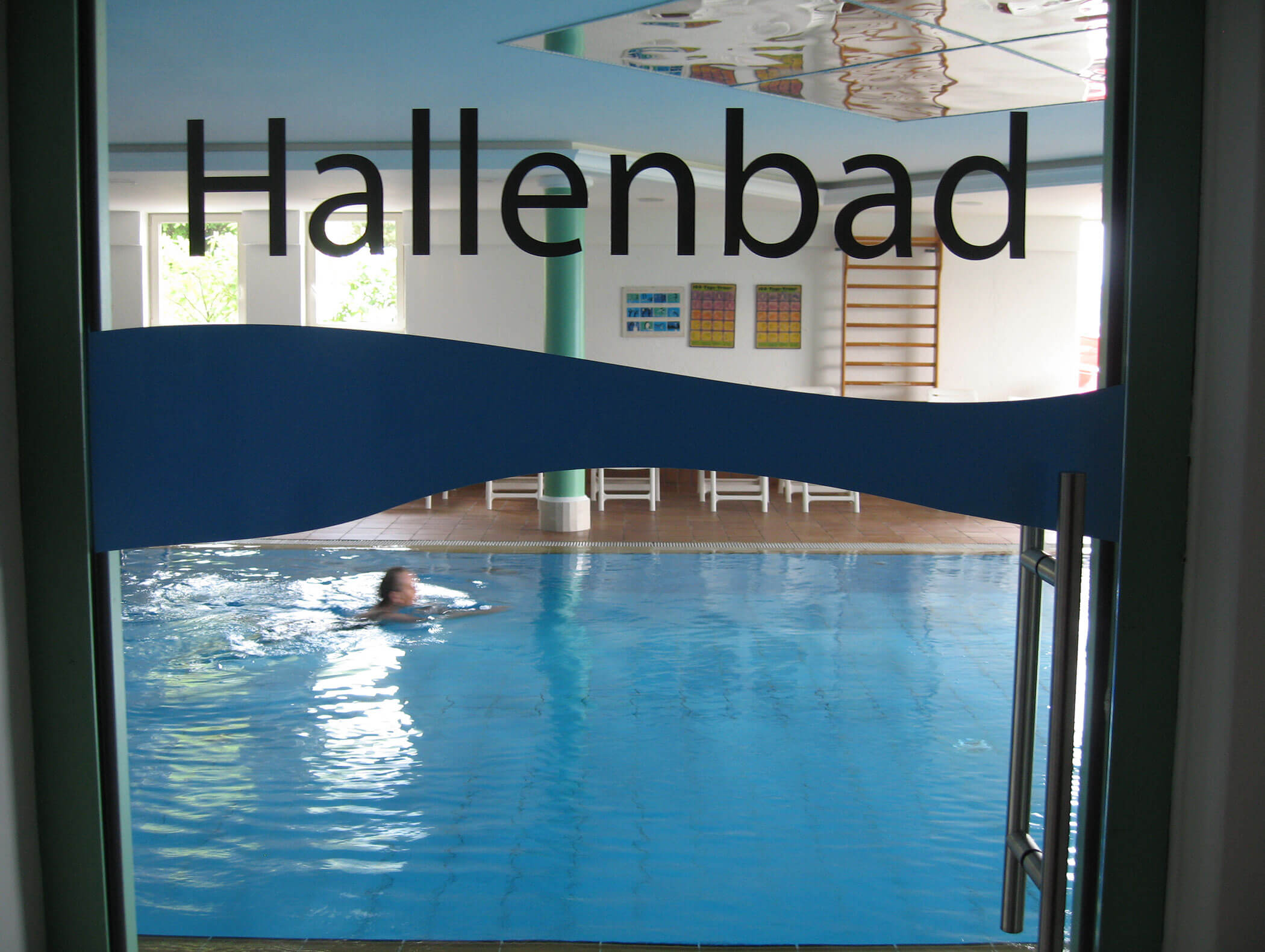 Piscina coperta con un nuotatore, vista attraverso una porta di vetro con la scritta Hallenbad a caratteri cubitali. - Wandergasthof Steinegger