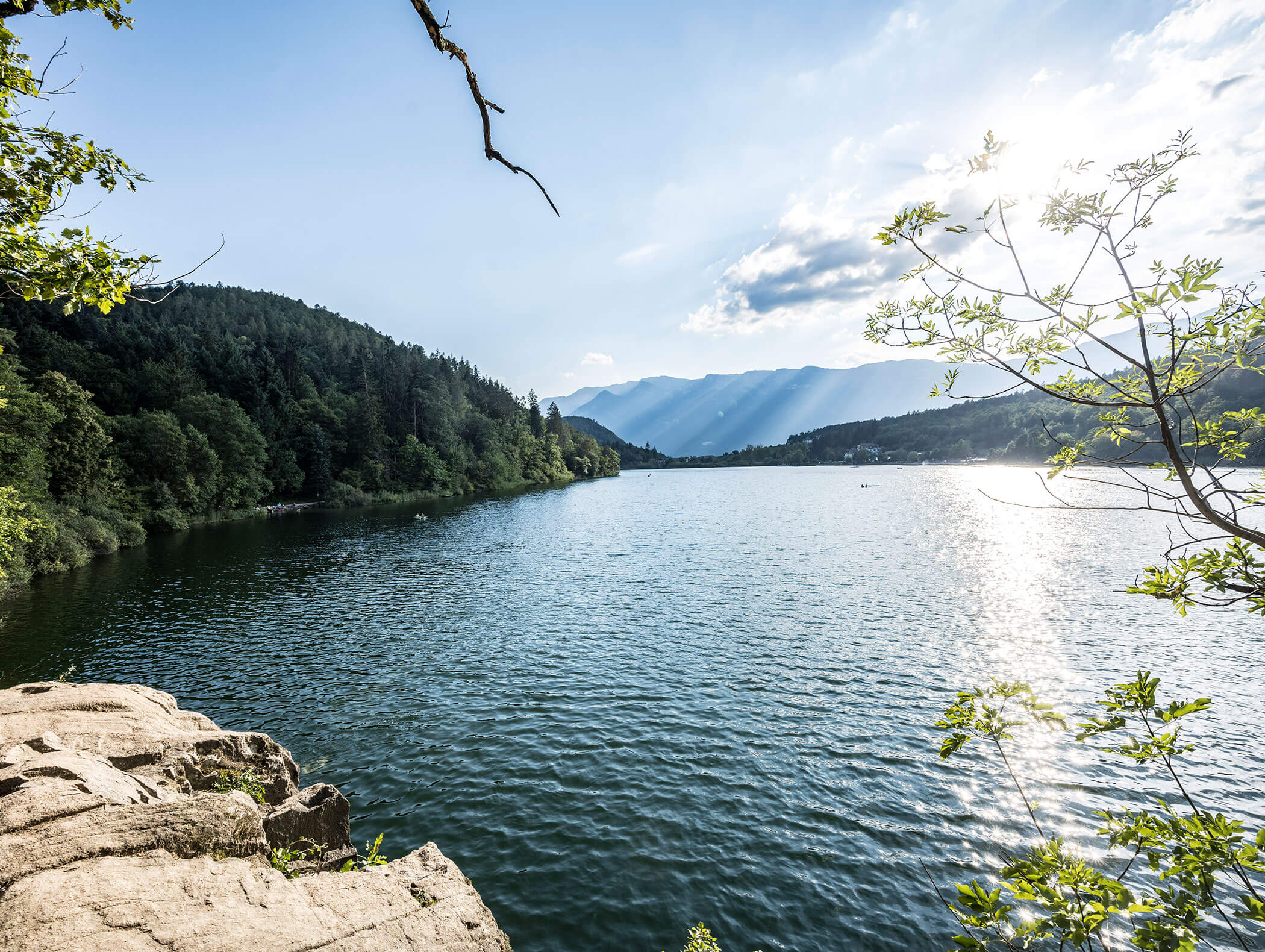 Un lago tranquillo circondato da colline boscose, con la luce del sole che si riflette sull'acqua e le montagne in lontananza. - Wandergasthof Steinegger