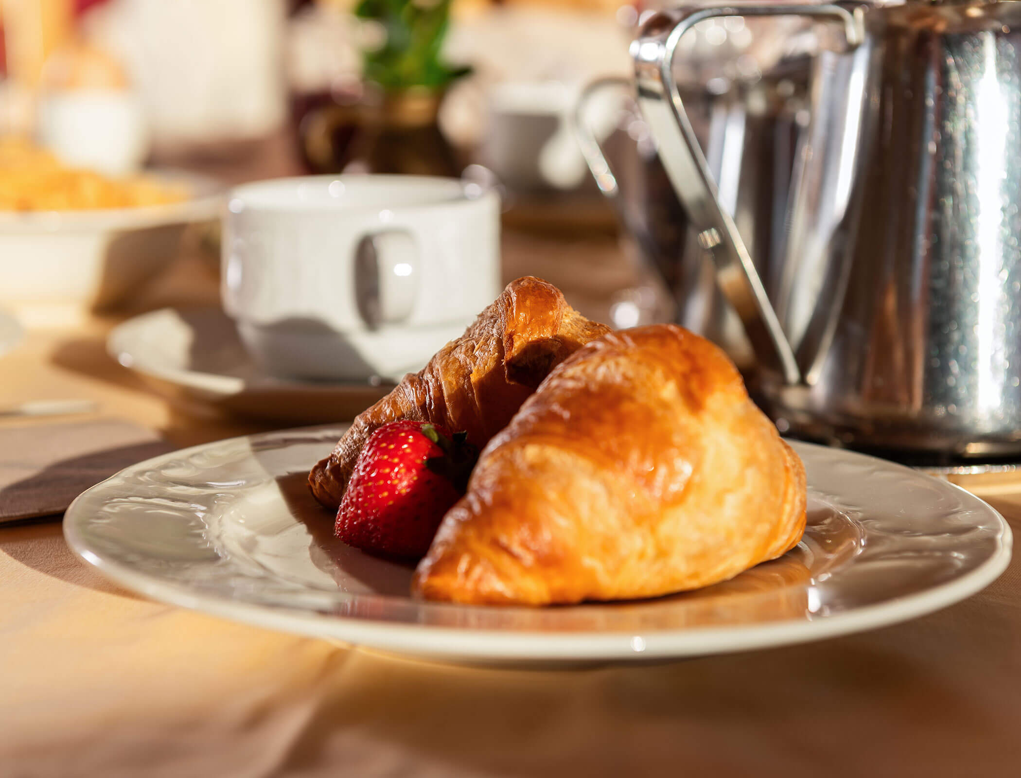 Un piatto con due croissant e fragole, con una tazza da caffè e una teiera sullo sfondo. - Wandergasthof Steinegger