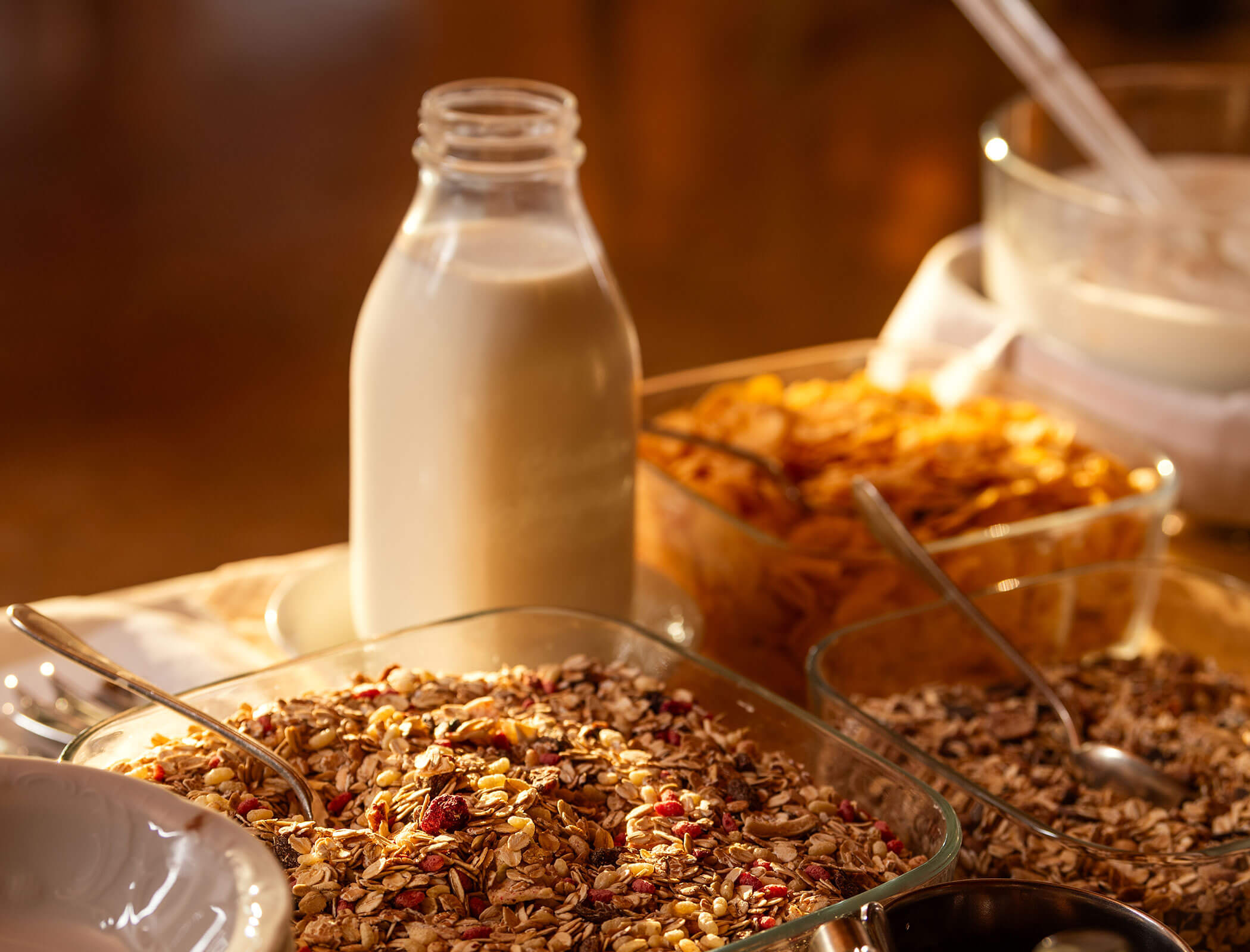 Bottiglia di latte in vetro con ciotole di granola, cornflakes e muesli su un tavolo da colazione. - Wandergasthof Steinegger
