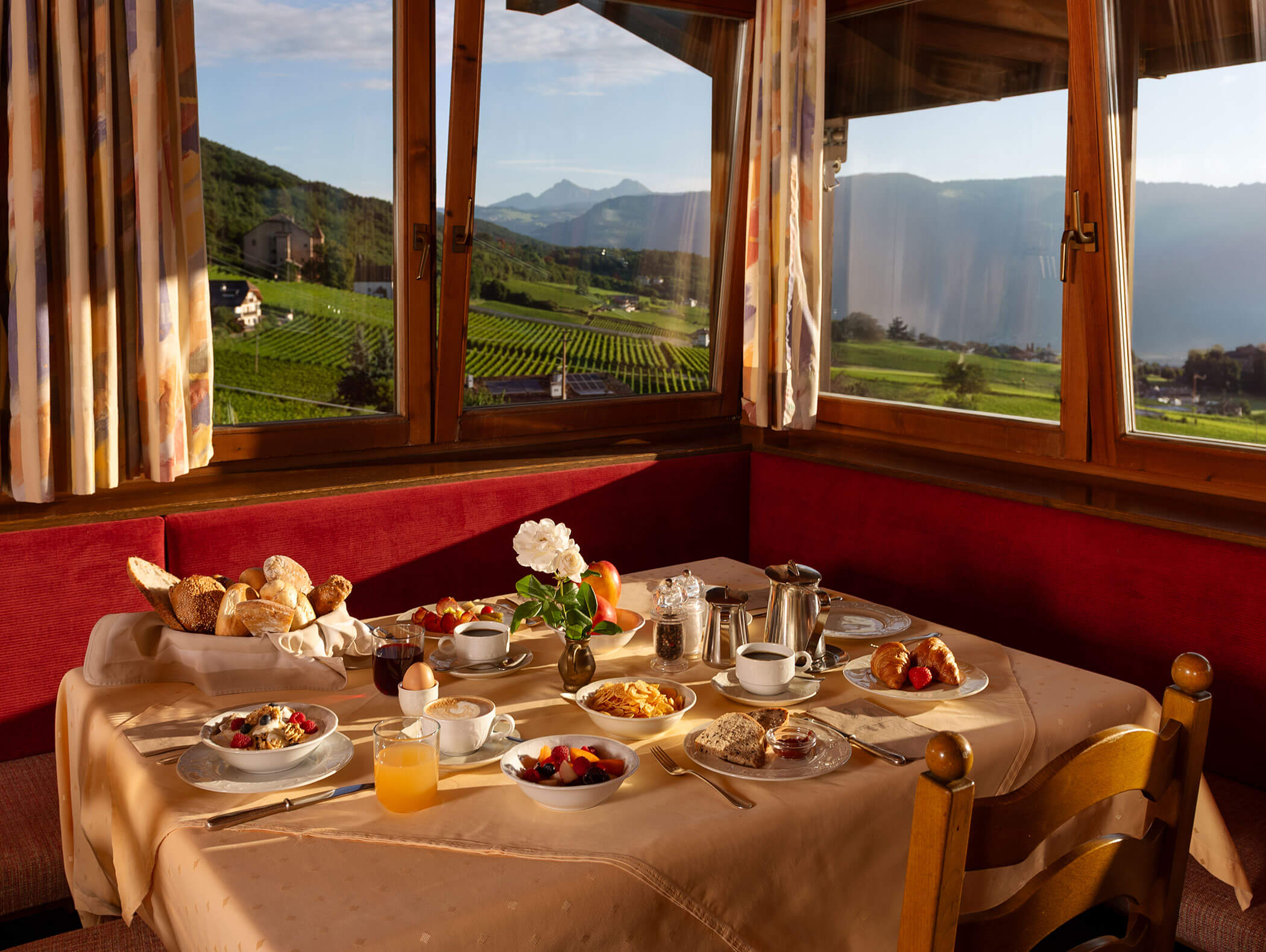 Un tavolo per la colazione con dolci, frutta e caffè accanto a una finestra con vista sulle colline verdi e sui vigneti. - Wandergasthof Steinegger