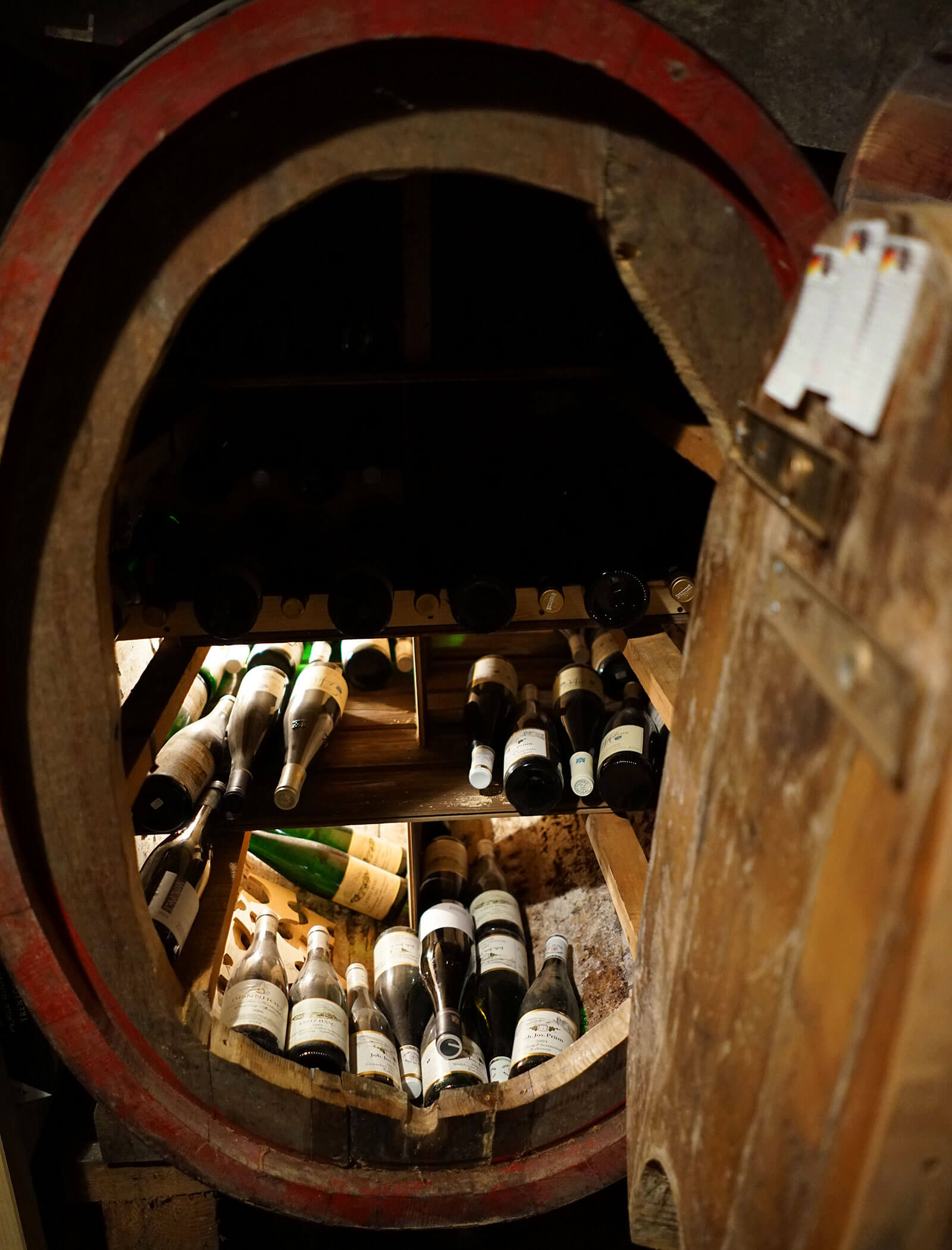 Bottiglie di vino impilate all'interno di una grande botte di legno aperta in una cantina poco illuminata. - Wandergasthof Steinegger