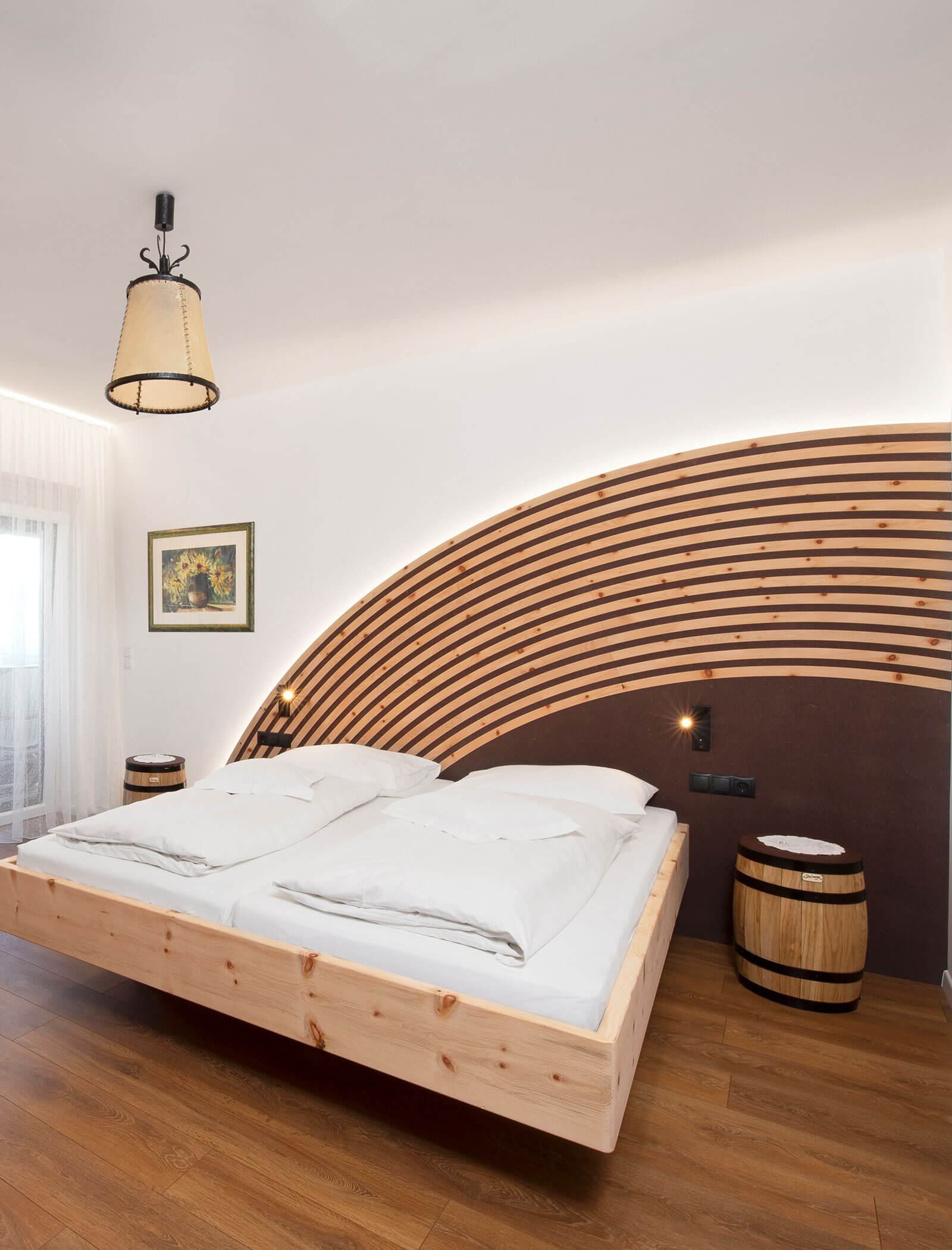 Modernes Schlafzimmer mit einem schwebenden Holzbett, Nachttischen aus Holz und einer geschwungenen Akzentwand aus Holzlatten. - Wandergasthof Steinegger