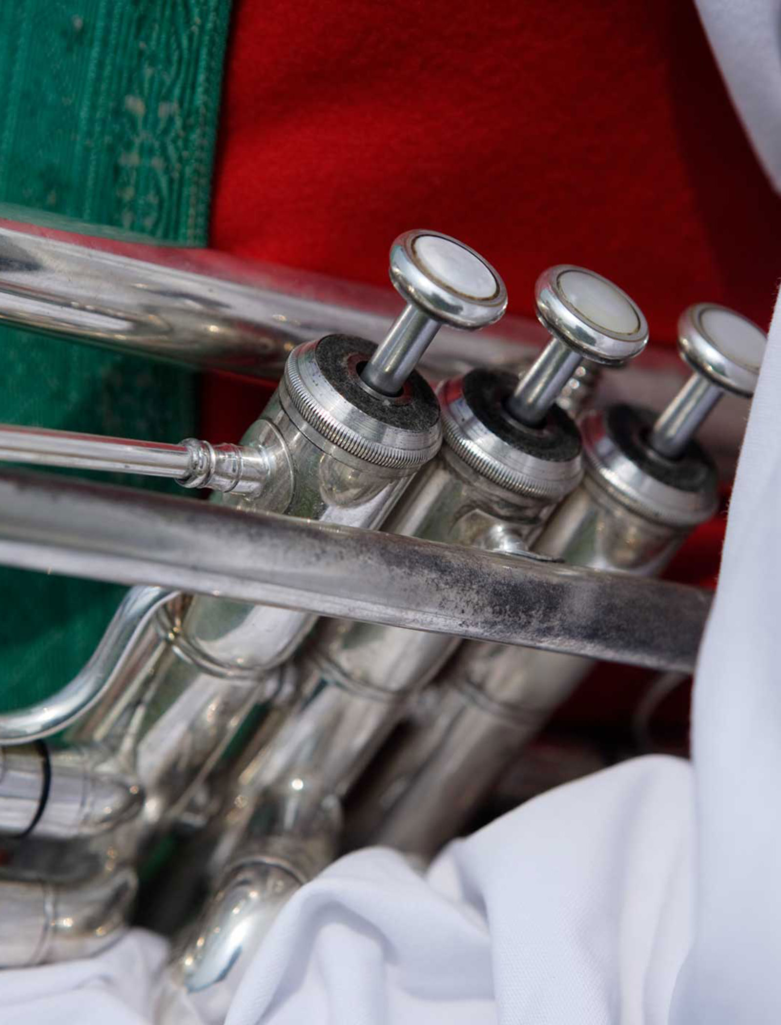 Close-up of a silver trumpets valves against a background of red, green, and white fabric. - Wandergasthof Steinegger