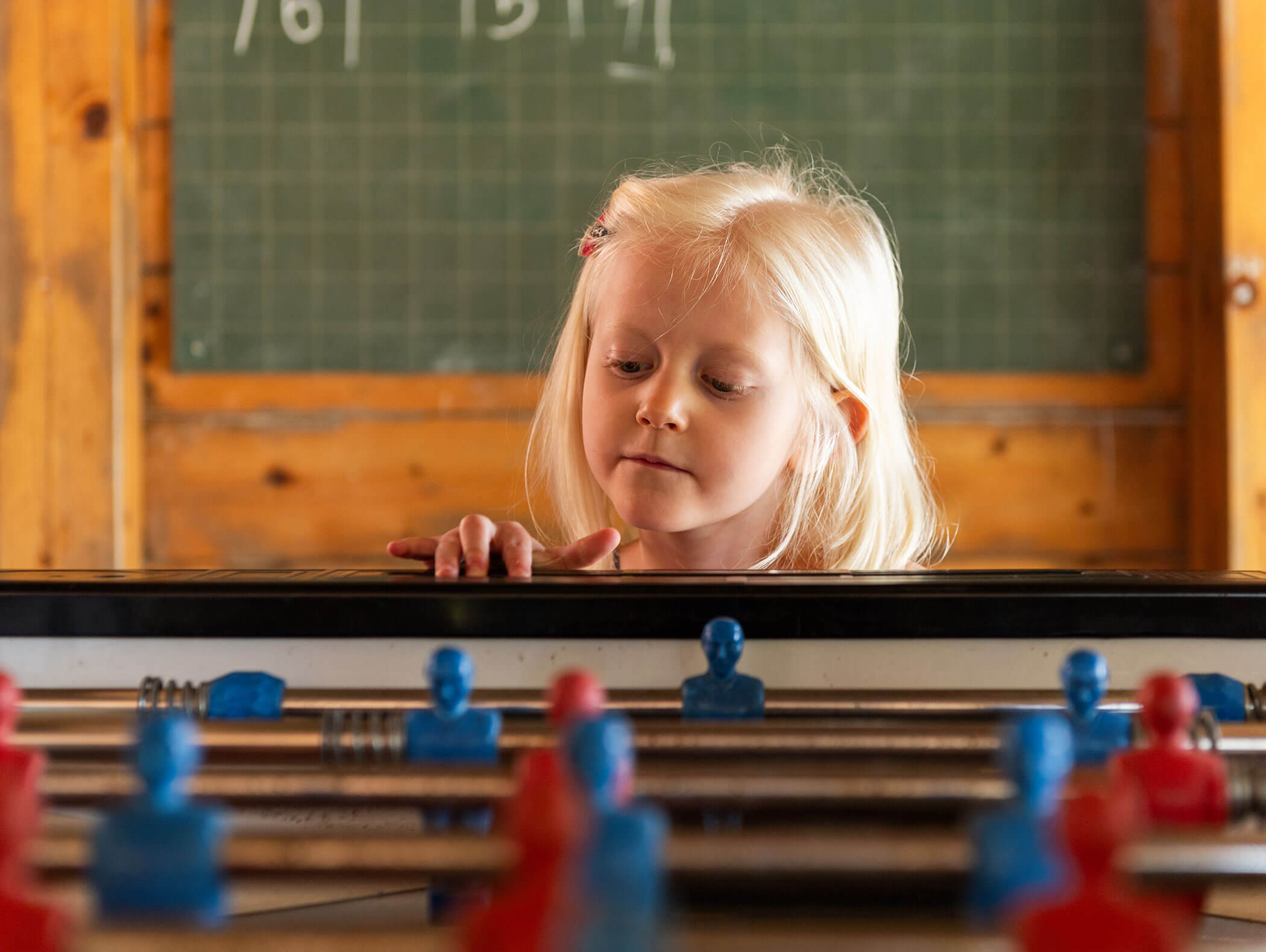 Young girl with blonde hair playing table football, chalkboard in the background. - Wandergasthof Steinegger
