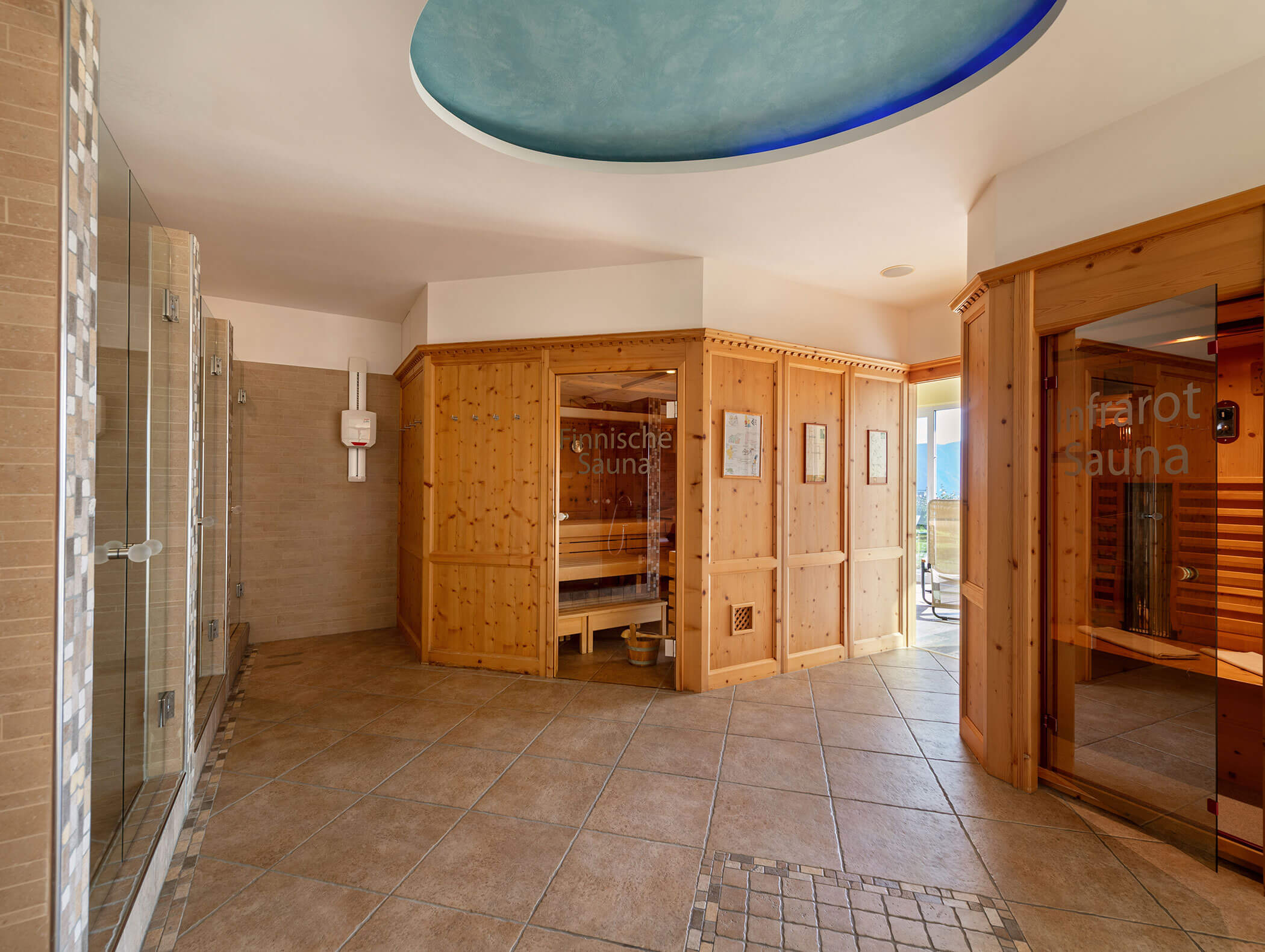 Ein Wellness-Raum mit Holzsaunen, gefliestem Boden, Glastüren und einem blauen Oval an der Decke. - Wandergasthof Steinegger