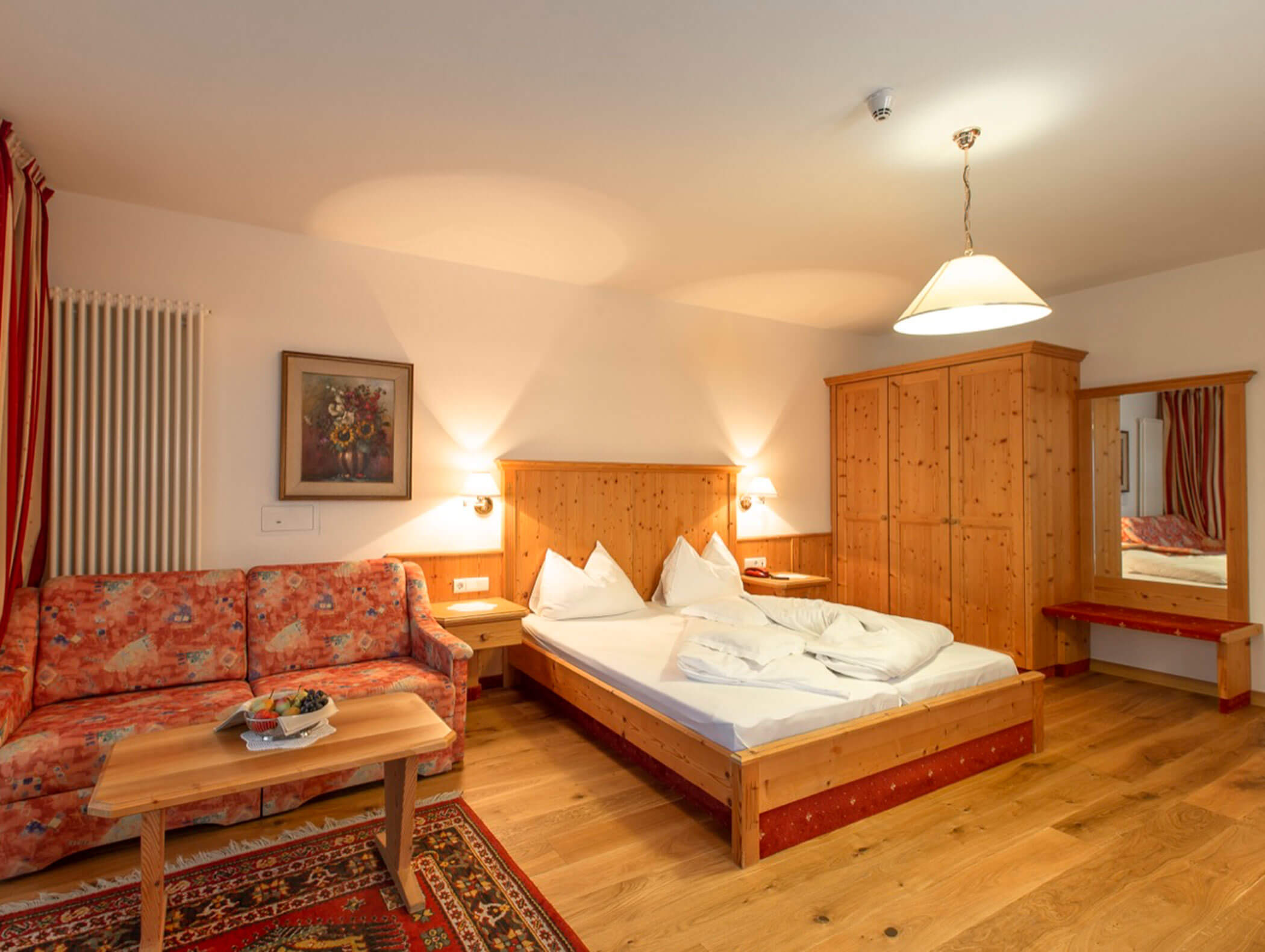 Cozy hotel room with wooden furniture, double bed, red-patterned sofa, and a small coffee table. - Wandergasthof Steinegger