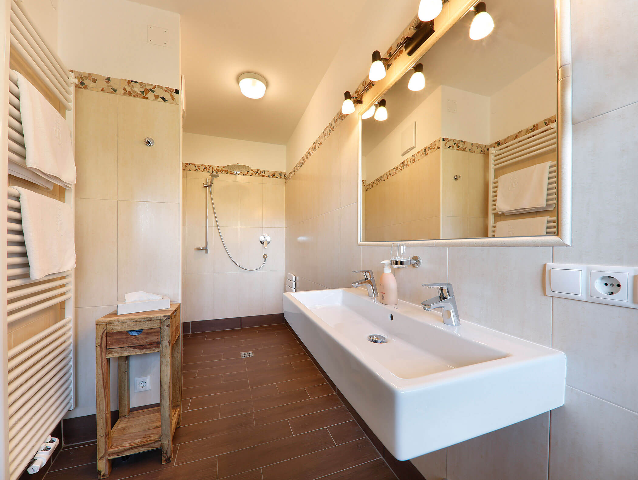 Spacious modern bathroom with double sink, shower area, large mirror, towel rack, and wooden accents. - Wandergasthof Steinegger