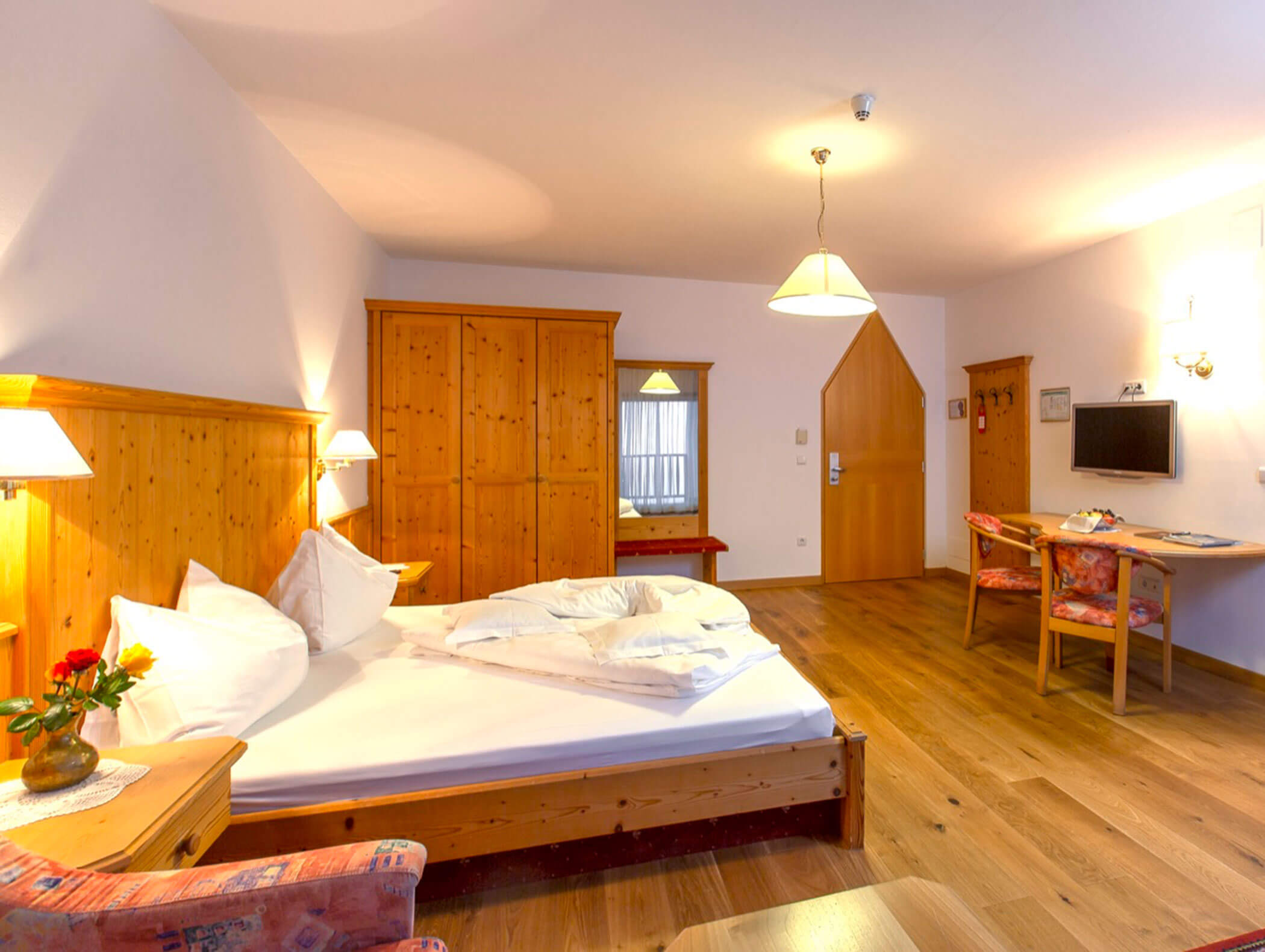 Cozy hotel room with wooden furniture, a double bed, desk, TV, chairs, and warm lighting. - Wandergasthof Steinegger