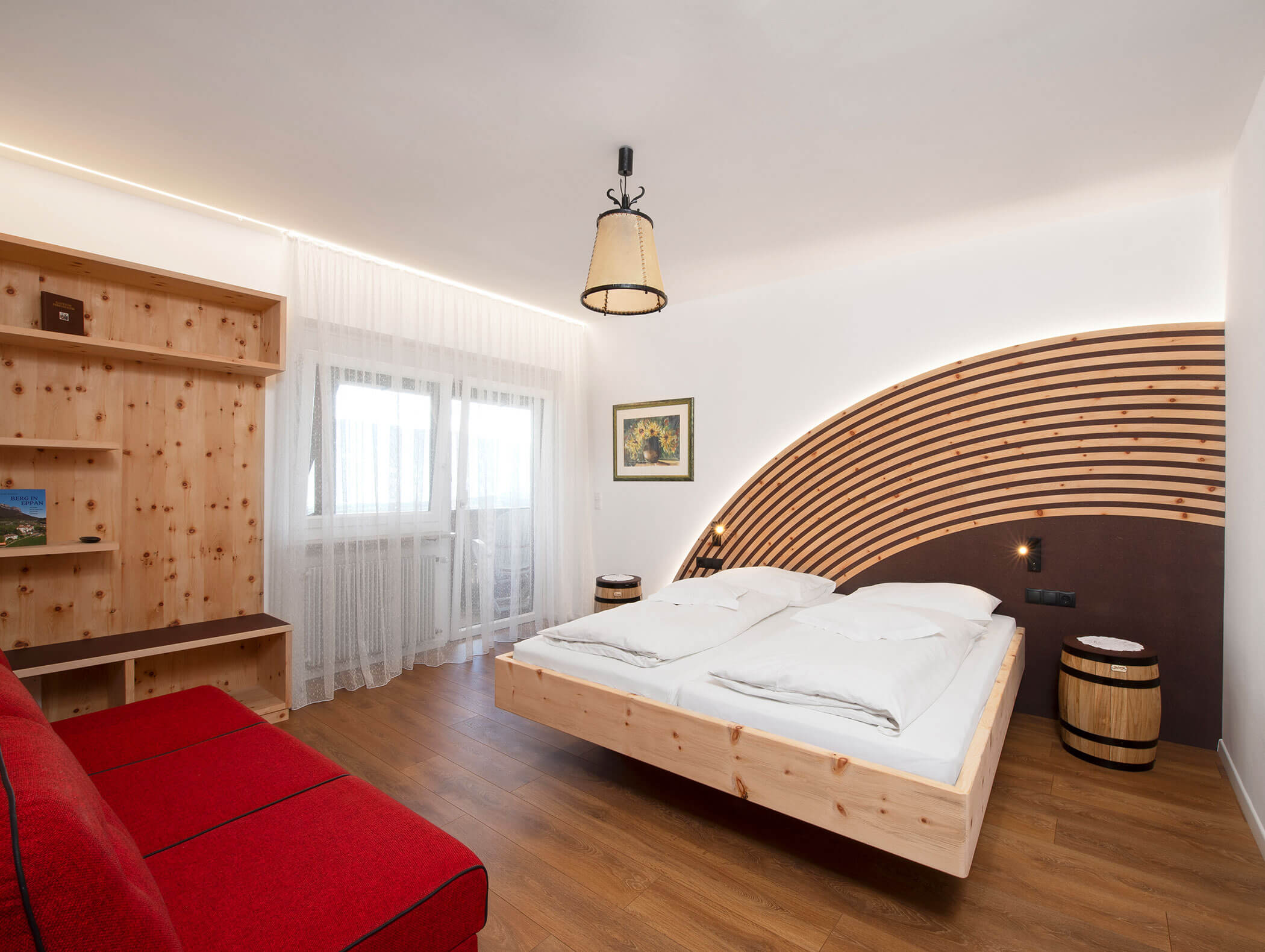 Modern bedroom with wood accents, a red sofa, floating bed, and a curved wooden headboard under soft lighting. - Wandergasthof Steinegger
