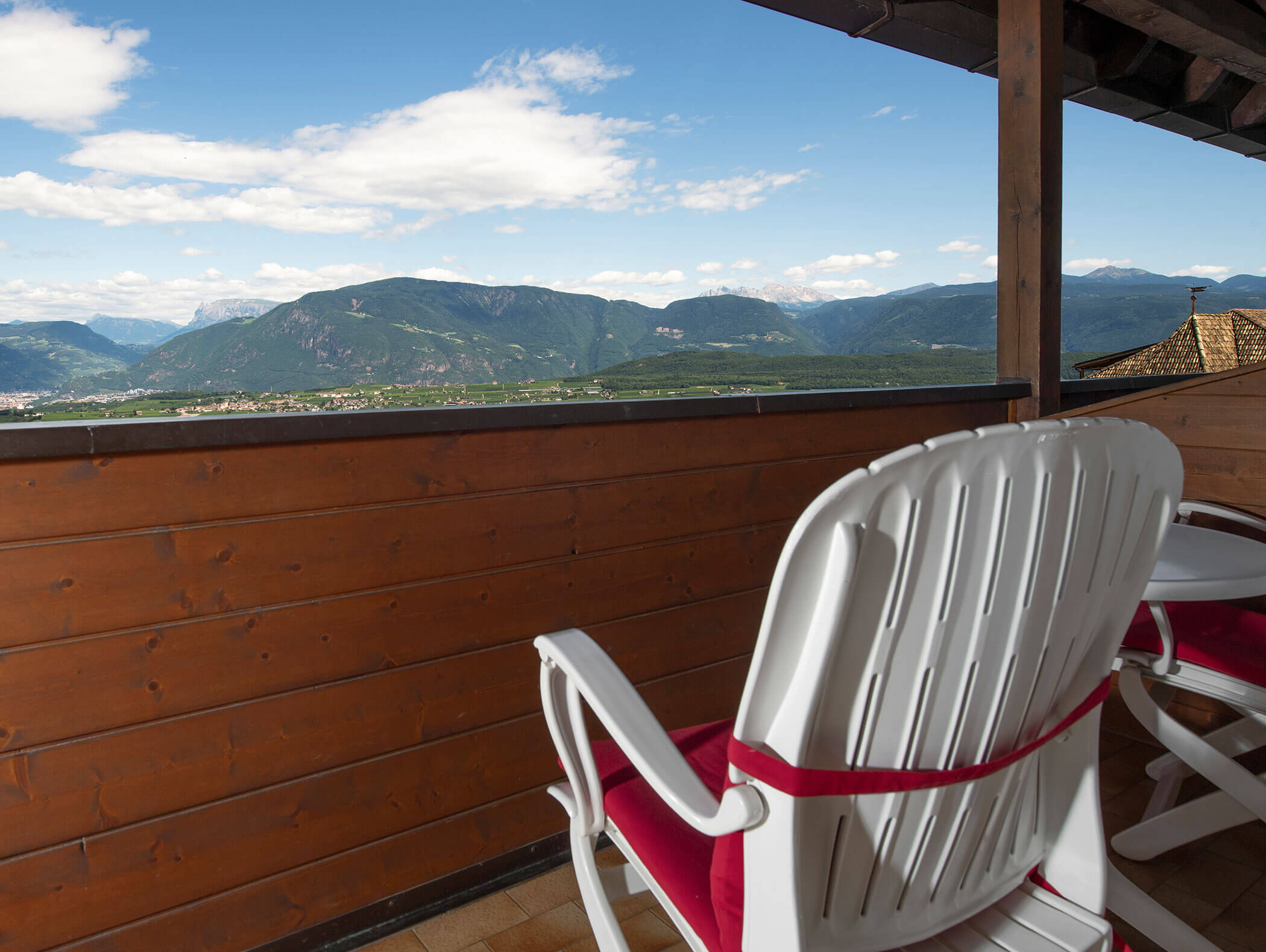 White plastic chair on a balcony with wooden railing, overlooking green mountains under a partly cloudy sky. - Wandergasthof Steinegger