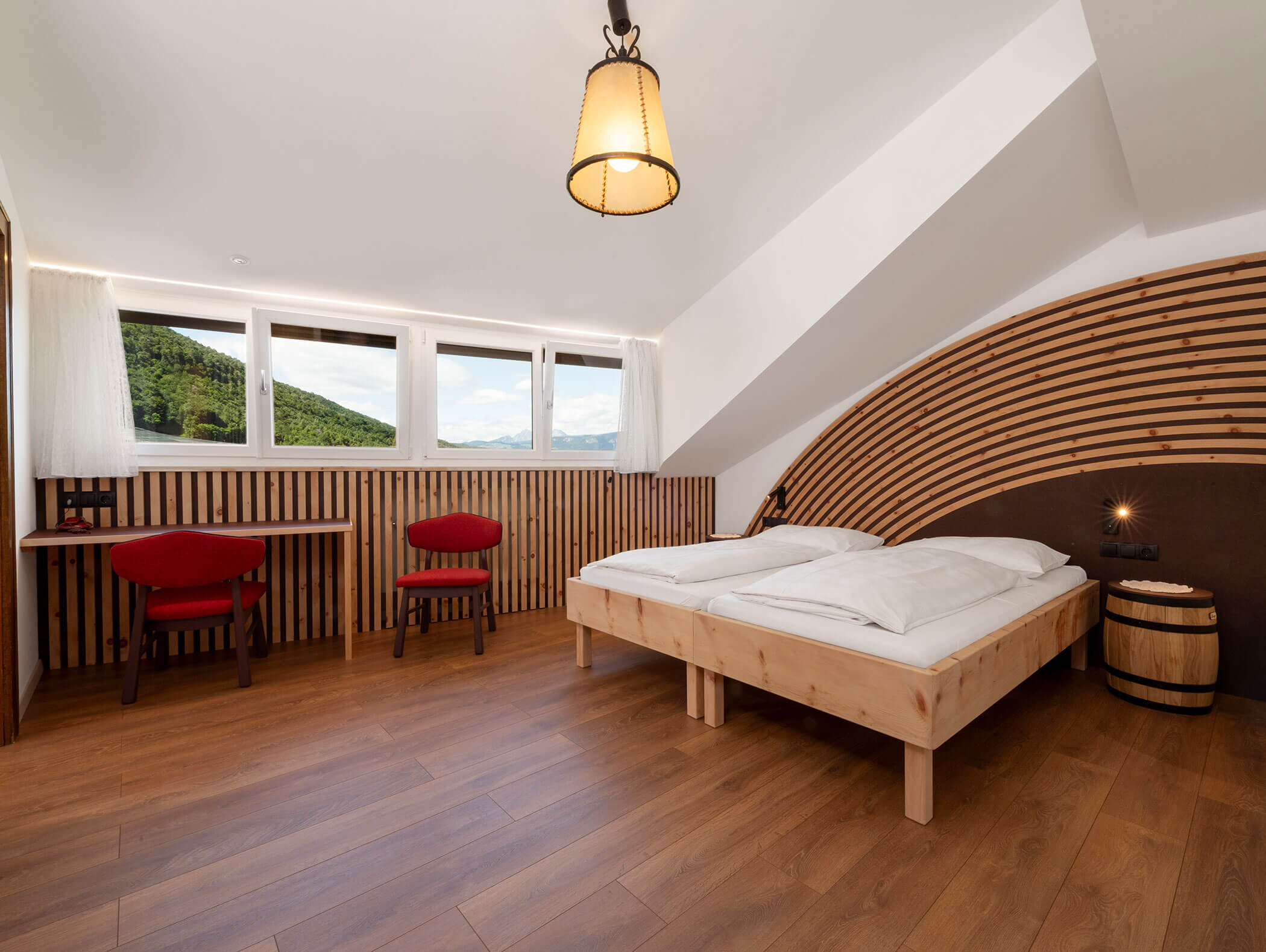 Minimalist hotel room with wooden accents, two red chairs, a desk, and a bed under a slanted ceiling. - Wandergasthof Steinegger