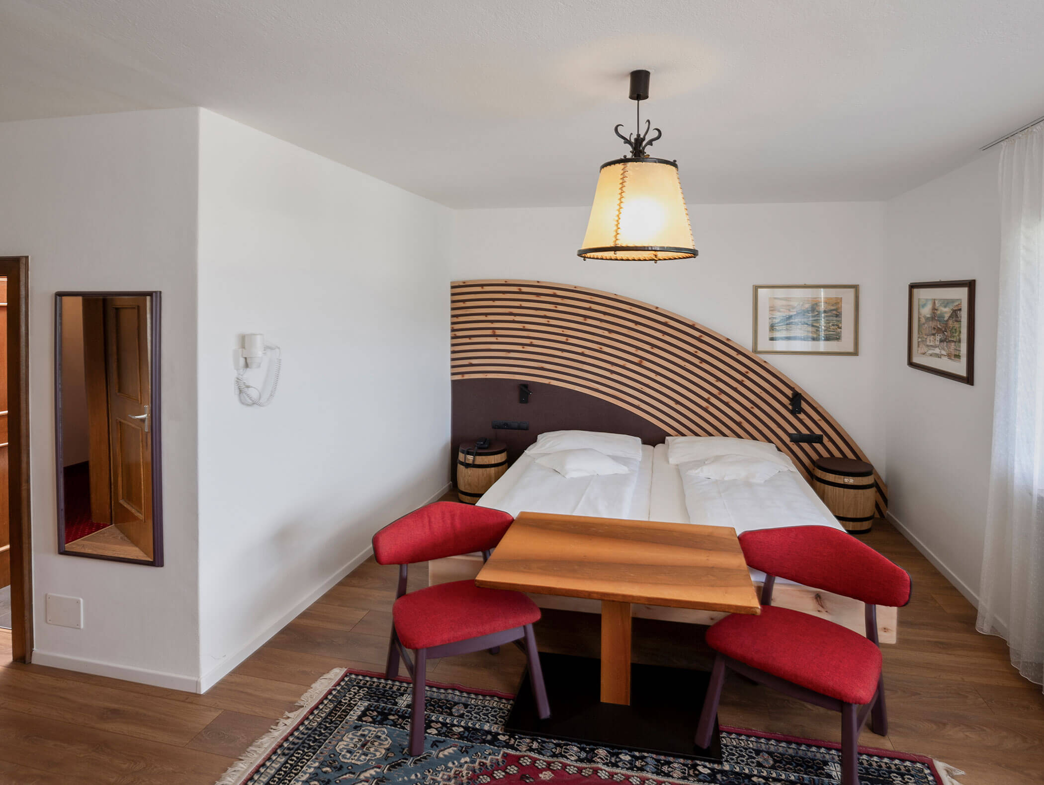 A modern hotel room with twin beds, a wooden table, red chairs, and a decorative headboard. - Wandergasthof Steinegger