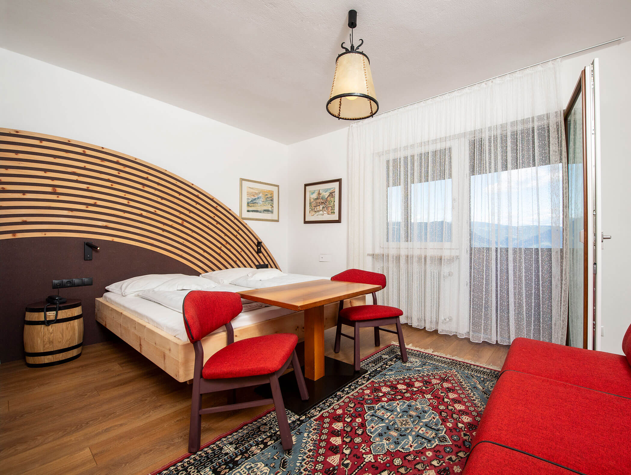 Cozy hotel room with a double bed, red chairs, a sofa, and large windows with sheer curtains. - Wandergasthof Steinegger